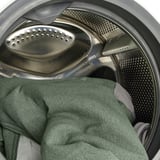 Washing machine drum with green towel, perforated metal interior, and rubber seal visible.