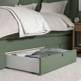 A green divan bed with open storage drawers under a folded blanket.