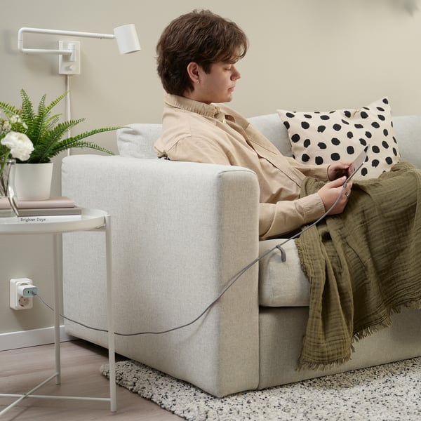 Person knitting on sofa with tablet, blanket, and book.