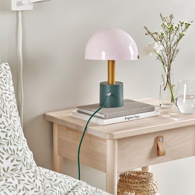A pastel lamp on a nightstand, powered by a usb-c cable, with books and a vase beside it.