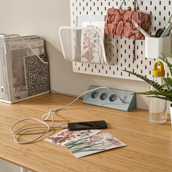 Wooden desk with phone charging via usb-c cable, organized with pegboard, plants, and documents.