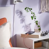 Minimalist nightstand with lamp, plant, books, and charging cable.