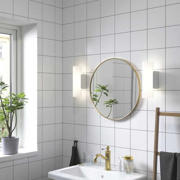 Modern bathroom with gold mirror, sink, lights, plant, and towels.