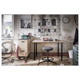 Industrial workspace with LINNMON desk, stool, clock, decor, and bicycle.