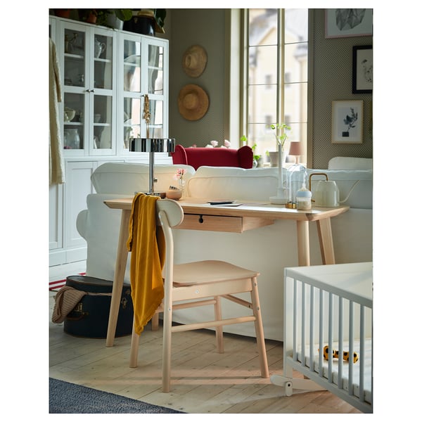 A light-colored wooden desk with drawers, part of the LISABO series. The desk sits near a window in a cozy room.