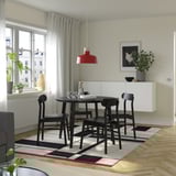 Modern dining area with black table and chairs, red pendant lamp, white walls, large window, patterned rug, and wall decorations.