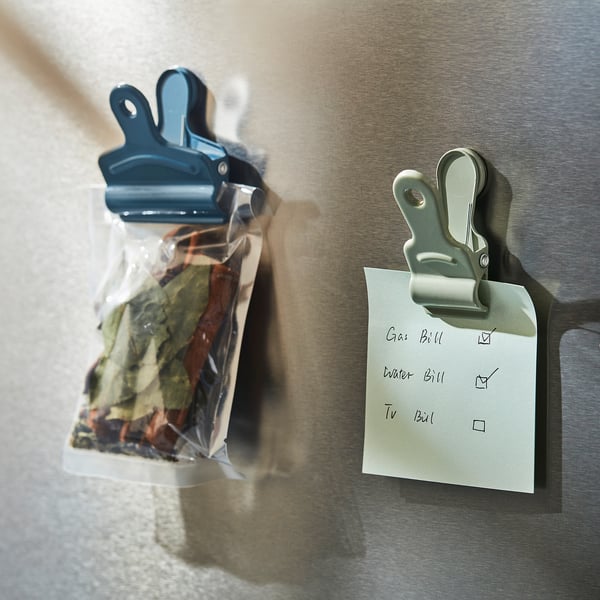 Two magnetic clips on a fridge: one seals a bagged herb, the other holds a to-do list.