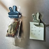 Two magnetic clips on a fridge: one seals a bagged herb, the other holds a to-do list.