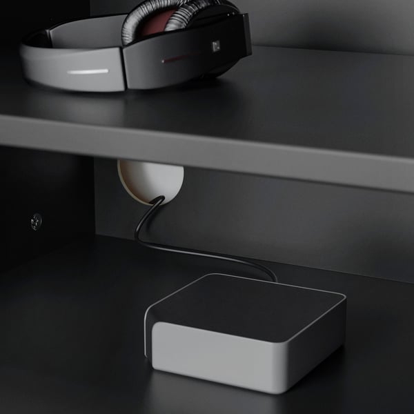 On sleek black desk, white headphones lay atop, connected to small speaker, tech setup arranged neatly.