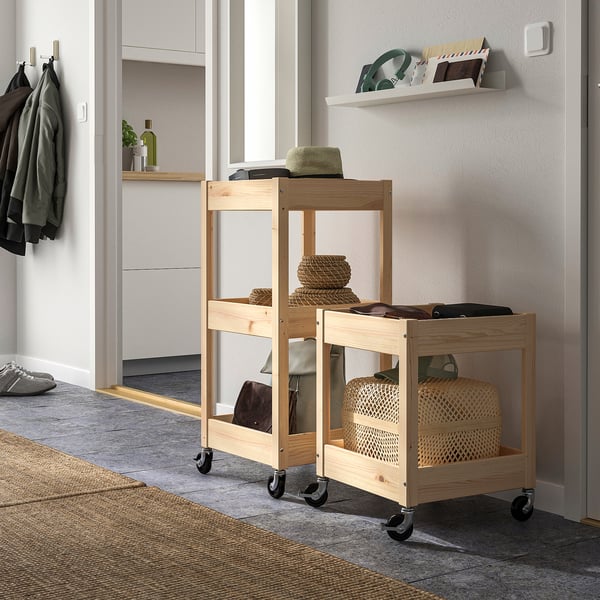 Wooden LOSHULT storage trolley with wheels, holding baskets and clothes, fitting neatly in a corner.