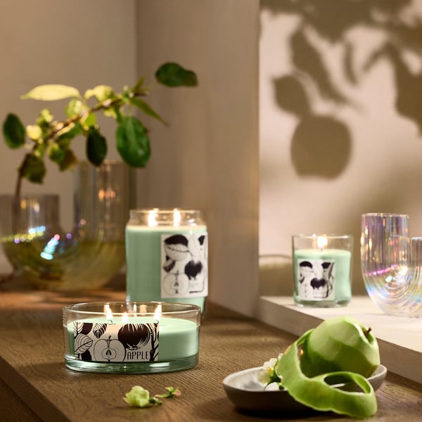 Three green apple candles on table with vases and plant.