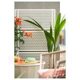 White privacy screen with lattice, steel & plastic, ideal for garden or terrace, with flowers on left, plant on right.