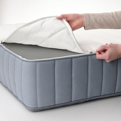 A person opens a gray LYNGÖR mattress, revealing its quilted cover and supportive interior, showcasing comfort and design.
