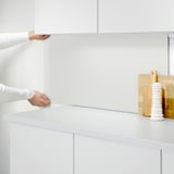 A person installs a LYSEKIL wall panel, protecting kitchen walls from splashes and grease, shown in white.