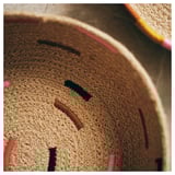 Hand-embroidered natural jute basket, browns with pink & black accents. Circular, rustic design.