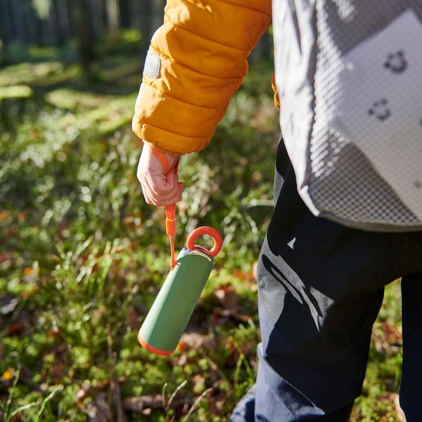 Hand in yellow jacket holds green-red water bottle with orange light.