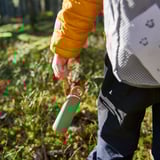 Hand in yellow jacket holds green-red water bottle with orange light.