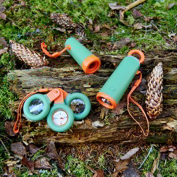 Green & orange outdoor gear set on log. Includes binoculars, compass, flashlight, & magnifying glass. Compact, bright colors.