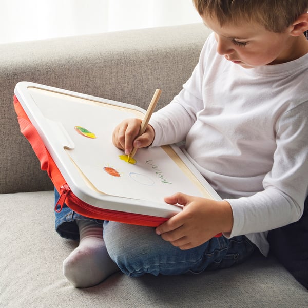 Child drawing with colored pencils on whiteboard. Zipper pouch holds drawings, pencil sharpener, and brush.