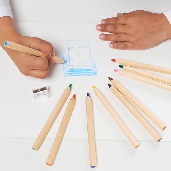 Childs hands drawing with colored pencils on white paper, surrounded by more pencils and a sharpener. Part of MÅLA creativity set.