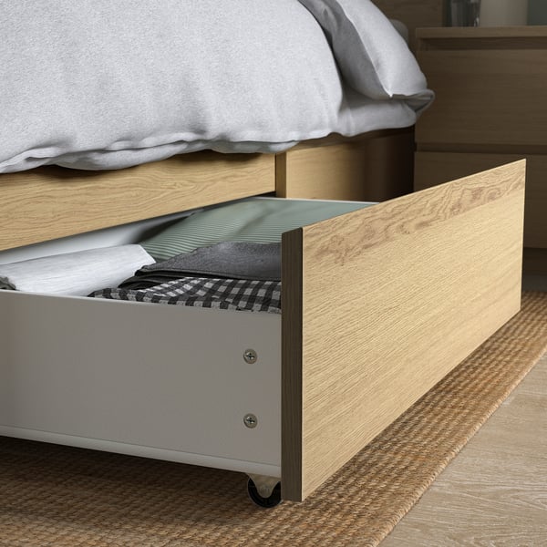 Open wooden drawer under bed with folded clothes, showing storage space.