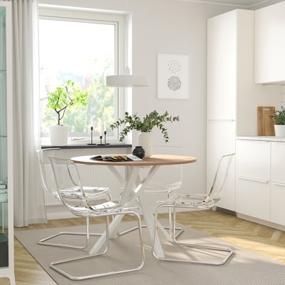 Modern dining area with large window, white cabinet, round wooden table, and clear chairs. Simple, elegant design.