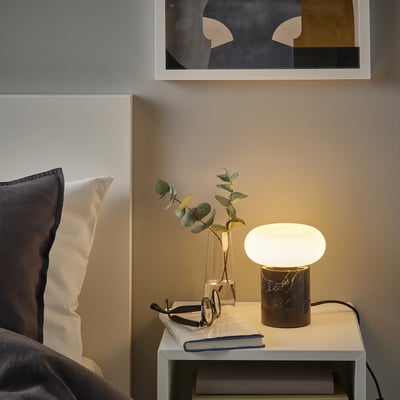 Lamp with black marble base and frosted glass shade on nightstand beside bed with gray/white pillows.