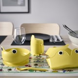 Yellow kids table set with bowls, mug, spoon, and bib. Bright, playful design. Size: smaller than regular dishes.