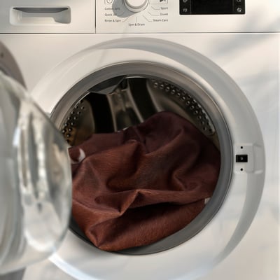 Washing machine with cowhide-patterned rug inside, ready for cleaning.