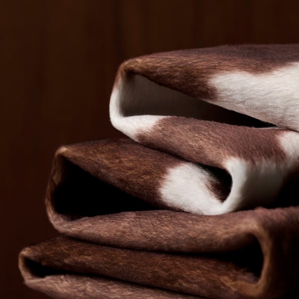 Cowhide patterned rug folded neatly. Soft, durable polyester material visible, ideal for modern or rustic settings.