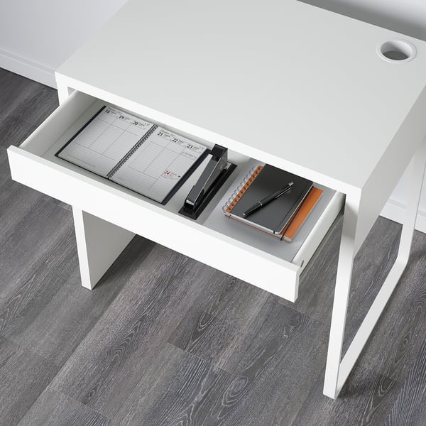 White desk with open drawer showing notebook, pens, and paper.