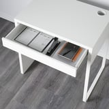 White desk with open drawer showing notebook, pens, and paper.