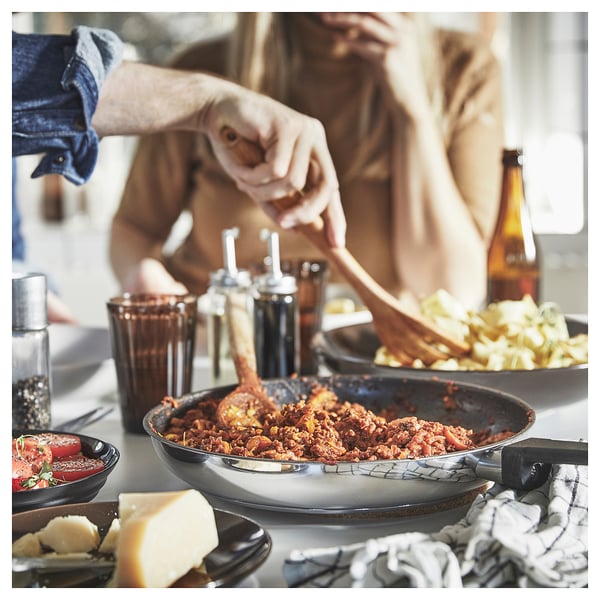 Kitchen scene with sizzling dish in MIDDAGSMAT pan. Hand stirring, seasonings, cheese, and beer bottle.