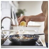 Cooking with lemon in non-stick pan, steam rising, person in brown sweater.