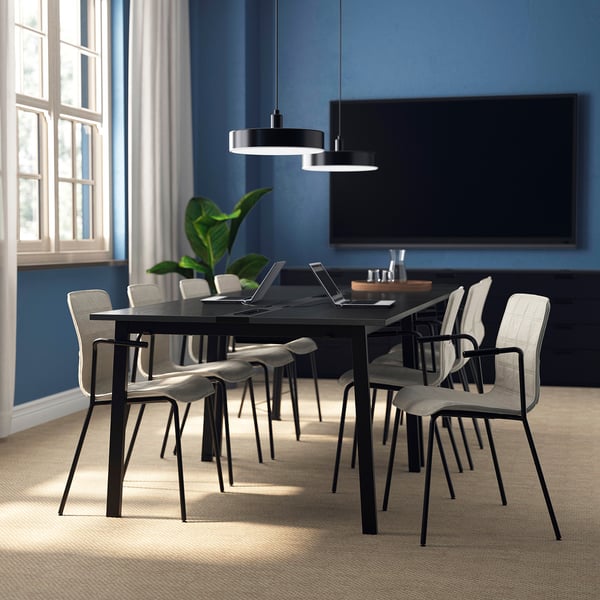 Modern conference room with black table, grey chairs, flat-screen tv, and plant.