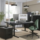 Modern office setup featuring MITTZON height-adjustable black desk with green chairs, two monitors, and sleek black pendant lights.