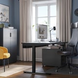 Modern home office with black desk, grey chair, yellow accent, window, and rug.