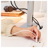Hand plugs white cord into desks power module.
