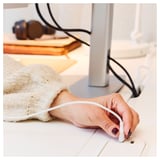 Persons hand holding white cord near white standing desk with cables, books, and knit item nearby.
