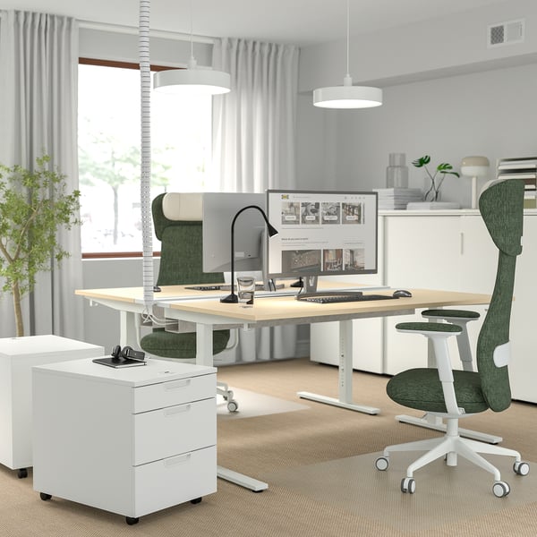 Modern home office with MITTZON desk, white with birch veneer. Green ergonomic chair, large dual monitors, and white file cabinet.