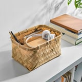 Wicker basket on desk, holding pens, notebooks, and headphones. Known for durable, handwoven bamboo, its a practical and stylish storage solution.