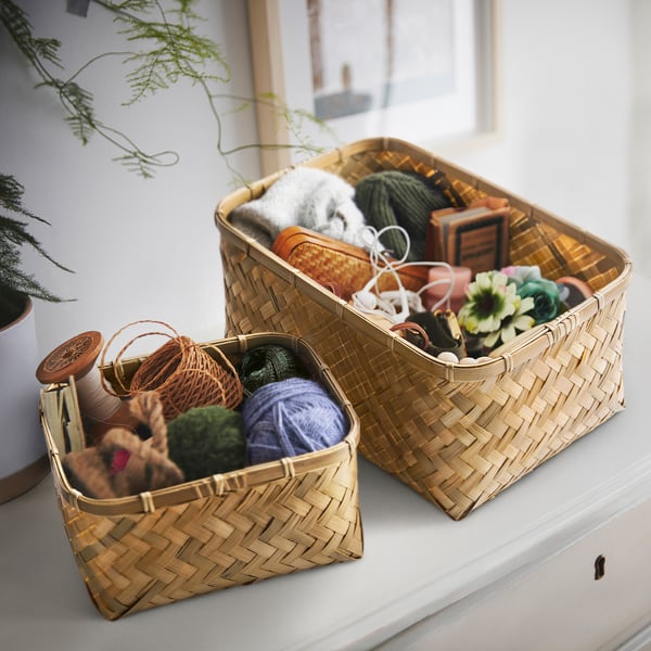 Two bamboo baskets on a shelf store yarn, knitting accessories, and small toys, showcasing organized craft storage.