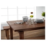 Modern wooden dining table set with clear glasses, white dishes, gray napkins, and a bottle with greens.