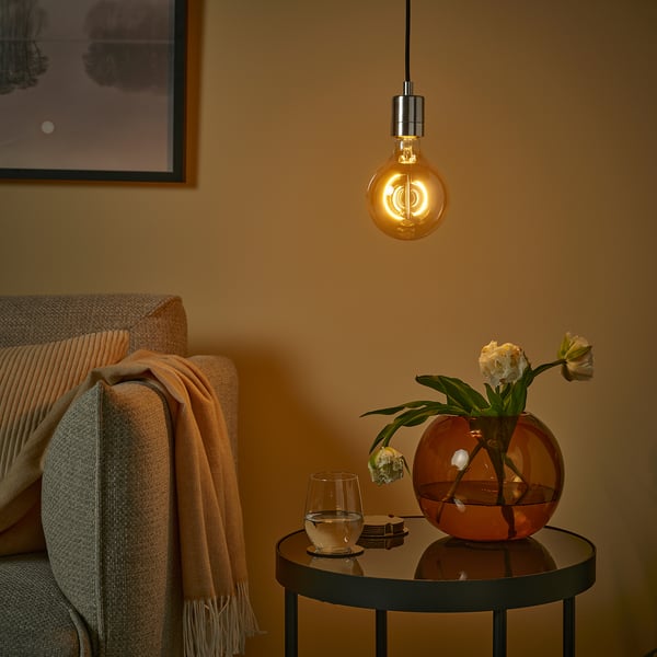 Cozy room with MOLNART bulb, red vase & flowers, glass, beige blanket, framed art, warm light.