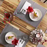 Two wooden tables set with MOTTAGA gray napkins, each holding a white plate topped with cake and candle, a red flower, and a clear glass.