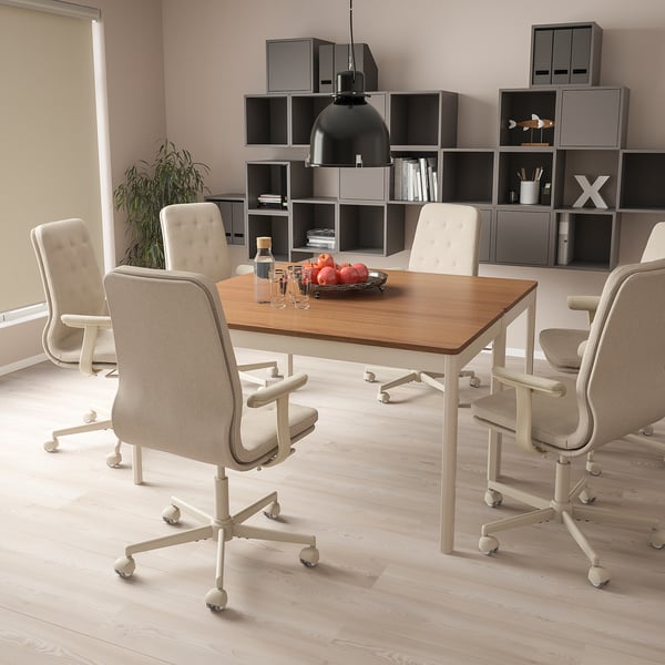 Modern office with light wood table, beige chairs, fruit bowl, and plant.