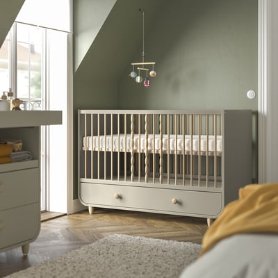Modern nursery with MYLLRA grey cot, adjustable base, green dresser, mobile, and cosy blanket.