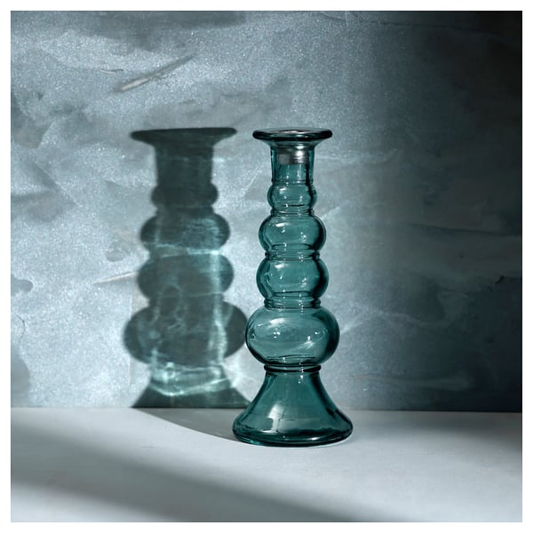 The MYRMOSAIK blue-green glass candlestick a bubble-textured design, casting intricate shadows.