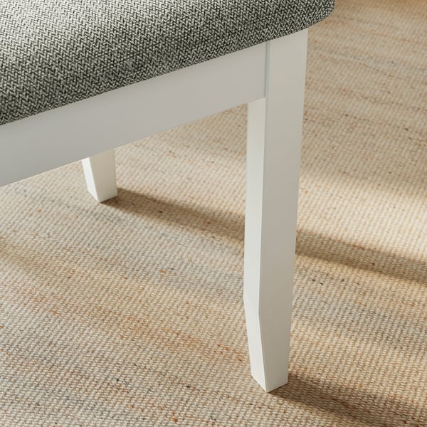 A corner of a well-crafted, modern farmhouse-style chair with a sturdy white wooden leg and a grey cushioned seat.