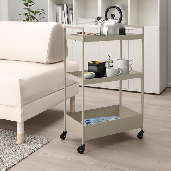 NISSAFORS beige trolley, small, 3-tiered, metal, near white sofa, holding kitchen items.